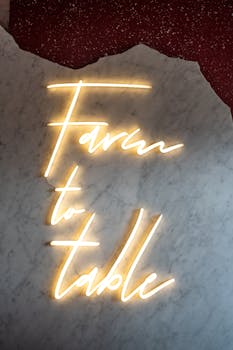Illuminated 'Farm to Table' neon sign on a textured marble wall, offering modern decor vibes.