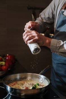 A chef seasons a dish in a modern kitchen, adding flavor to a culinary creation.