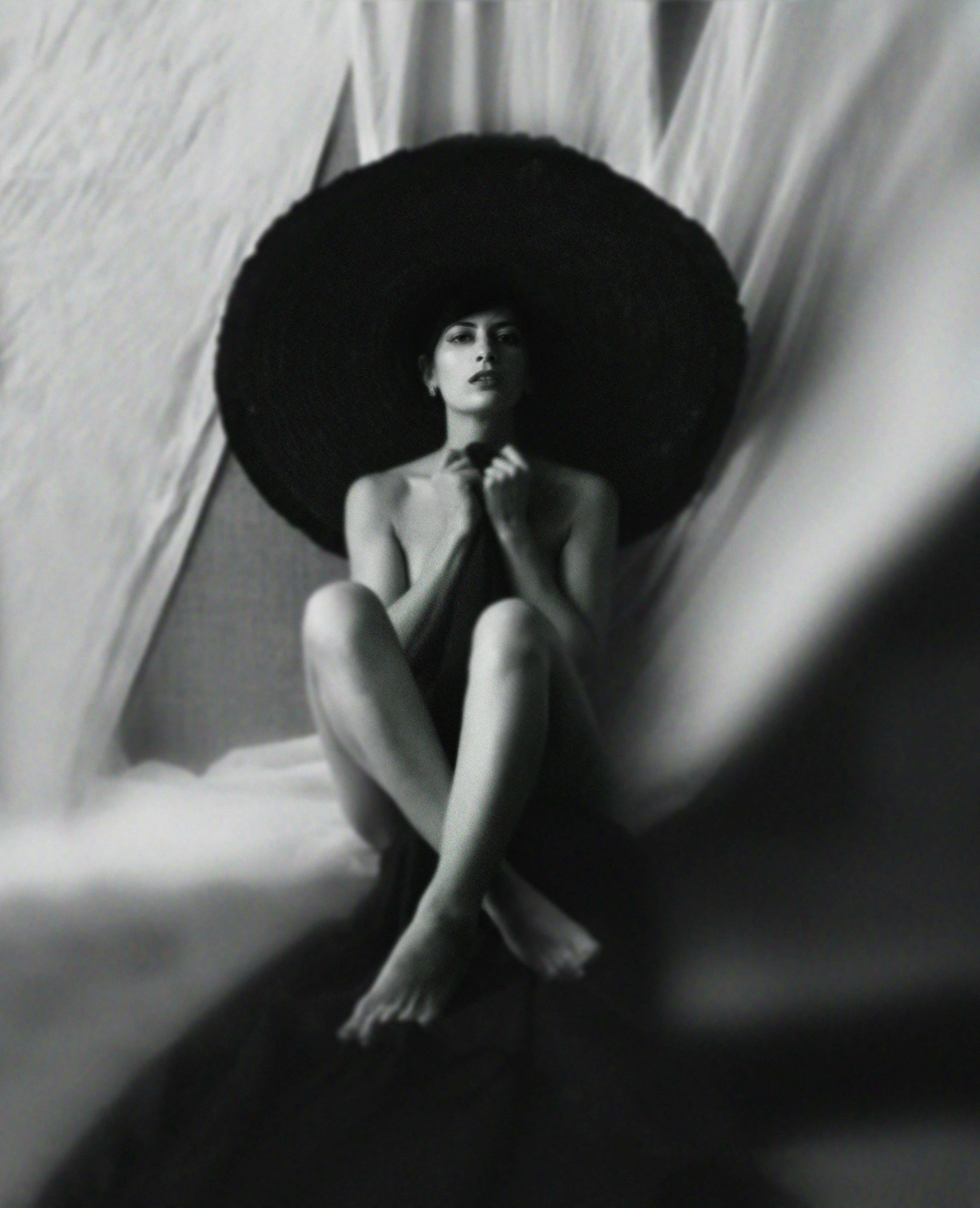 alluring young lady in hat sitting and covering body with blanket