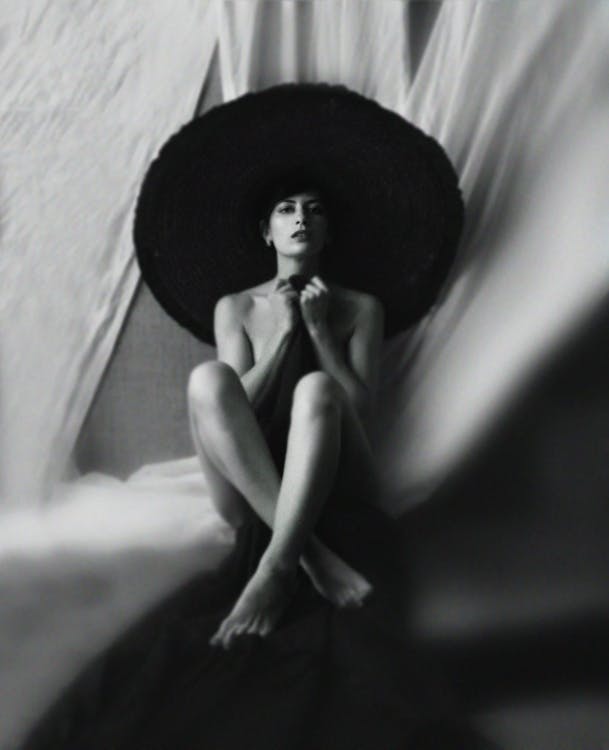 Очаровательная молодая дама в шляпе сидит и прикрывает тело одеялом