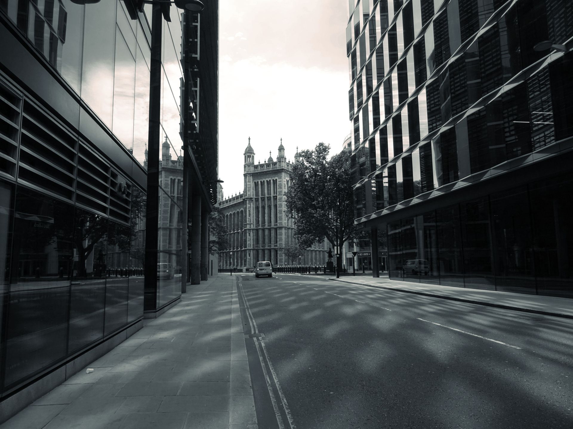 A serene urban street featuring modern and historic buildings with reflections and a cobblestone path.