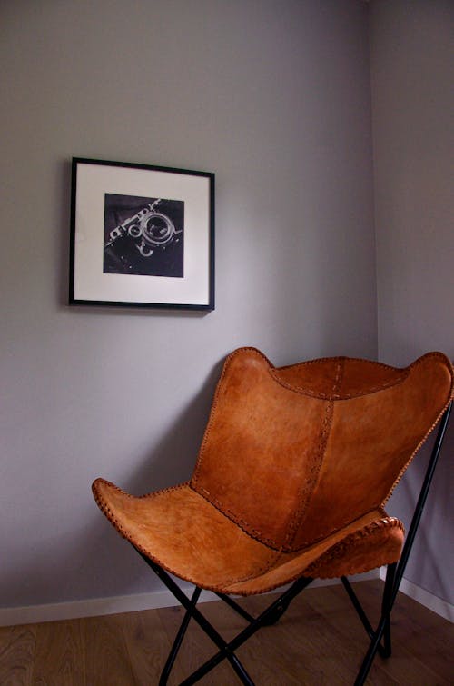 Comfortable retro leather armchair with metal legs placed in corner of cozy room near wall with framed picture