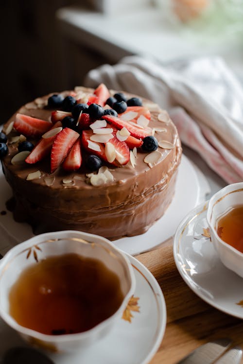 Free From above of delicious homemade chocolate cake decorated with fresh strawberries and blueberries served on table with elegant cups of tea in kitchen Stock Photo