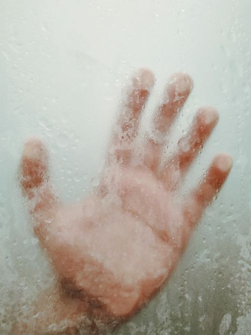 Free Through glass hand of crop unrecognizable person touching misted window with drops during rain Stock Photo