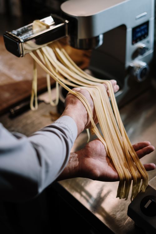 Free Hands guiding fresh pasta through a pasta machine in a home kitchen setting. Stock Photo
