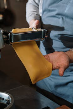 Close-up of fresh pasta being prepared with a manual pasta machine in a kitchen setting.