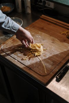 Hand making fresh pasta on wooden cutting board in kitchen setting.