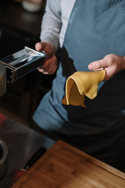 Close-up of a chef using a pasta maker, crafting fresh dough in a modern kitchen setting.