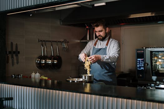Male chef cooking pasta in a modern kitchen. Professional culinary setting.