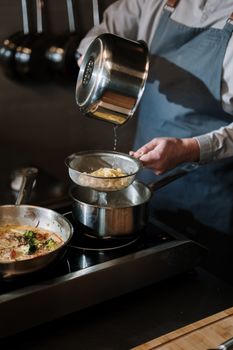 Close-up of a chef straining pasta over a stovetop, showcasing professional cooking skills.