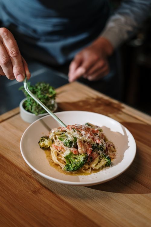 Free A delicious plate of Italian pasta garnished with fresh herbs and broccoli, prepared by a male chef. Stock Photo