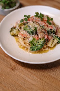 Close-up of creamy pasta with broccoli, salmon, and herbs on a white plate.