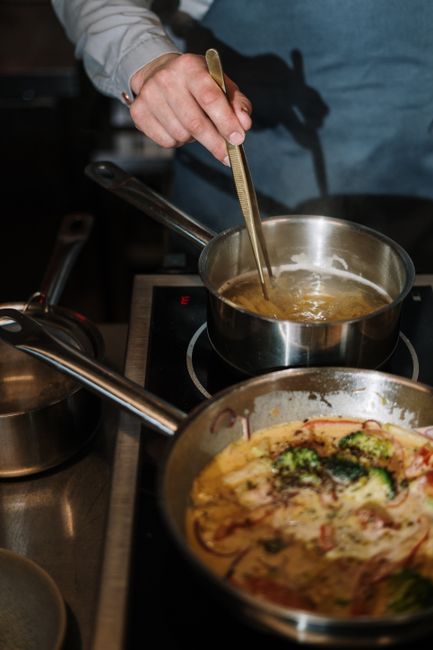 Cream sauce being poured into a pan of pasta dish`