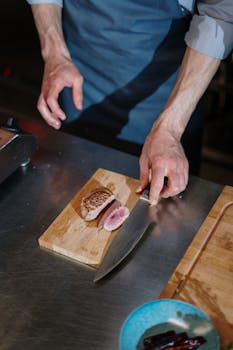A chef skillfully slices a steak on a wooden board in a professional kitchen setting.