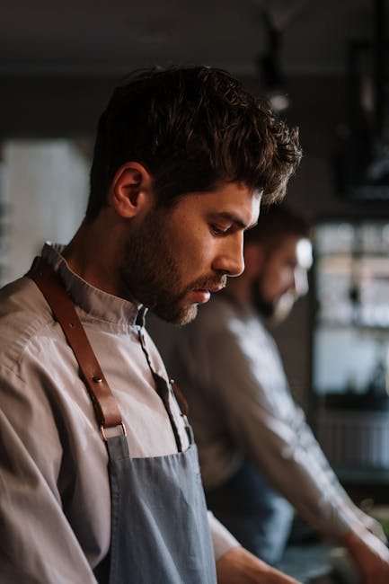 A young male chef focused on preparing a dish in a professional kitchen setting.