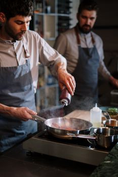 Two chefs in aprons work together in a modern kitchen, preparing food with focus and skill.