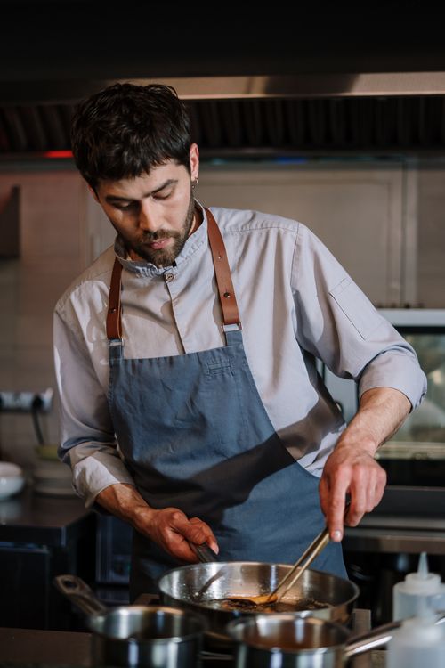 Free Chef in a blue apron focused on preparing food in a professional kitchen setting. Stock Photo