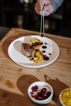 Close-up of a chef garnishing a gourmet steak and garnish plate in a professional kitchen.