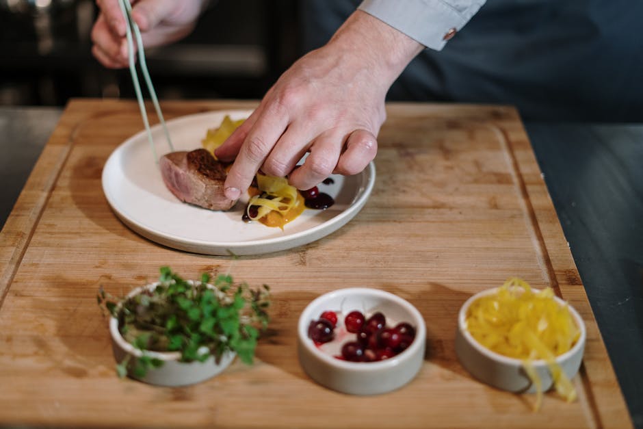 A professional chef in a modern kitchen, carefully plating a dish with tweezers and a focused expression.