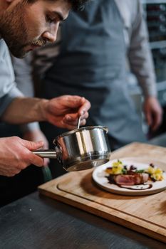 Chef adding final touches with sauce to a gourmet dish in a professional kitchen setting.