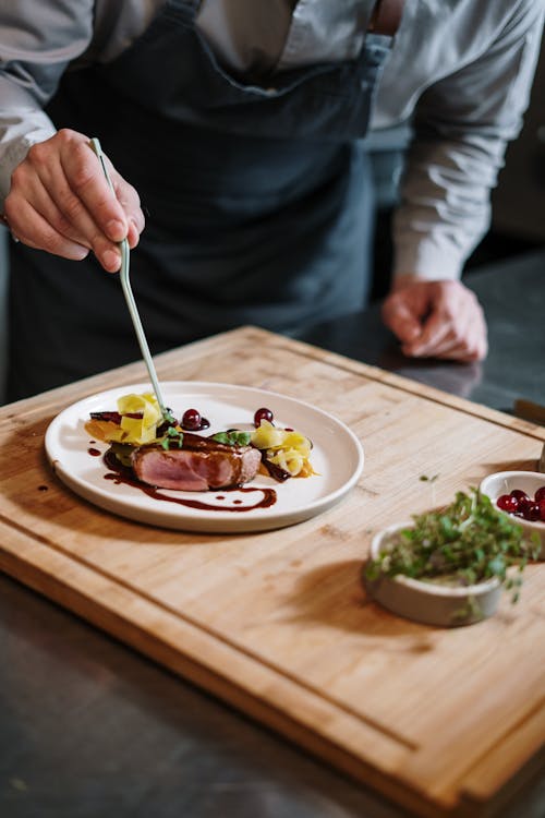 Person Holding Silver Fork and Knife Slicing Vegetable on White Ceramic Plate