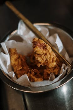 Close-up of crispy fried chicken in a bowl with a gold knife.