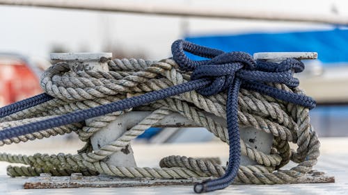 Close up of nautical knot ropes tied around metal bollard on modern ship deck