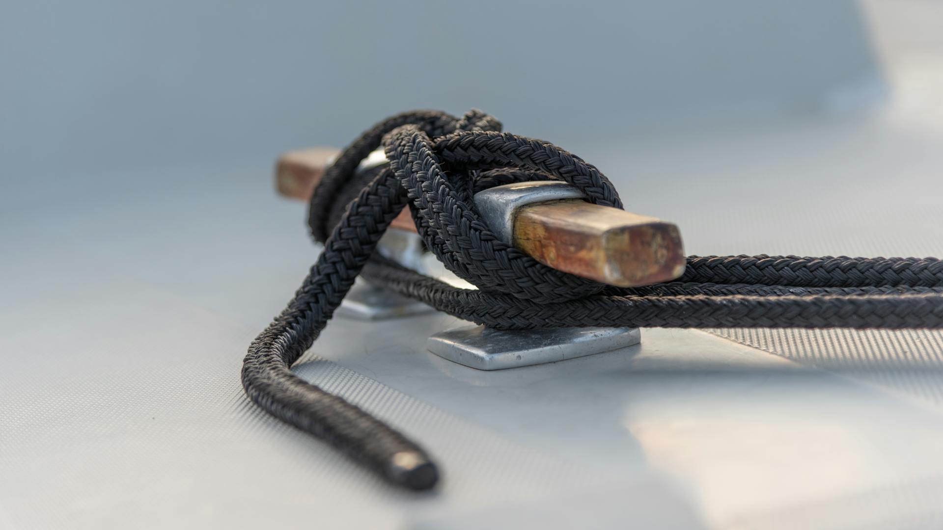 Detailed view of a black rope tied around a cleat on a boat deck, illustrating nautical safety.