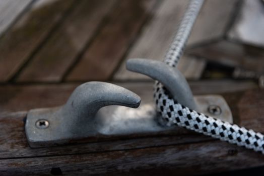 High angle of rope on metal mooring hook on wooden deck of boat
