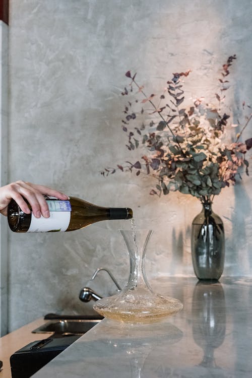 Person Pouring Wine on Clear Glass Bottle