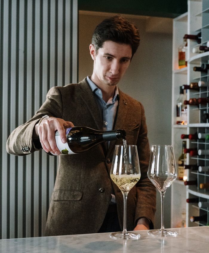 A sommelier pouring wine in front of a bottle wall