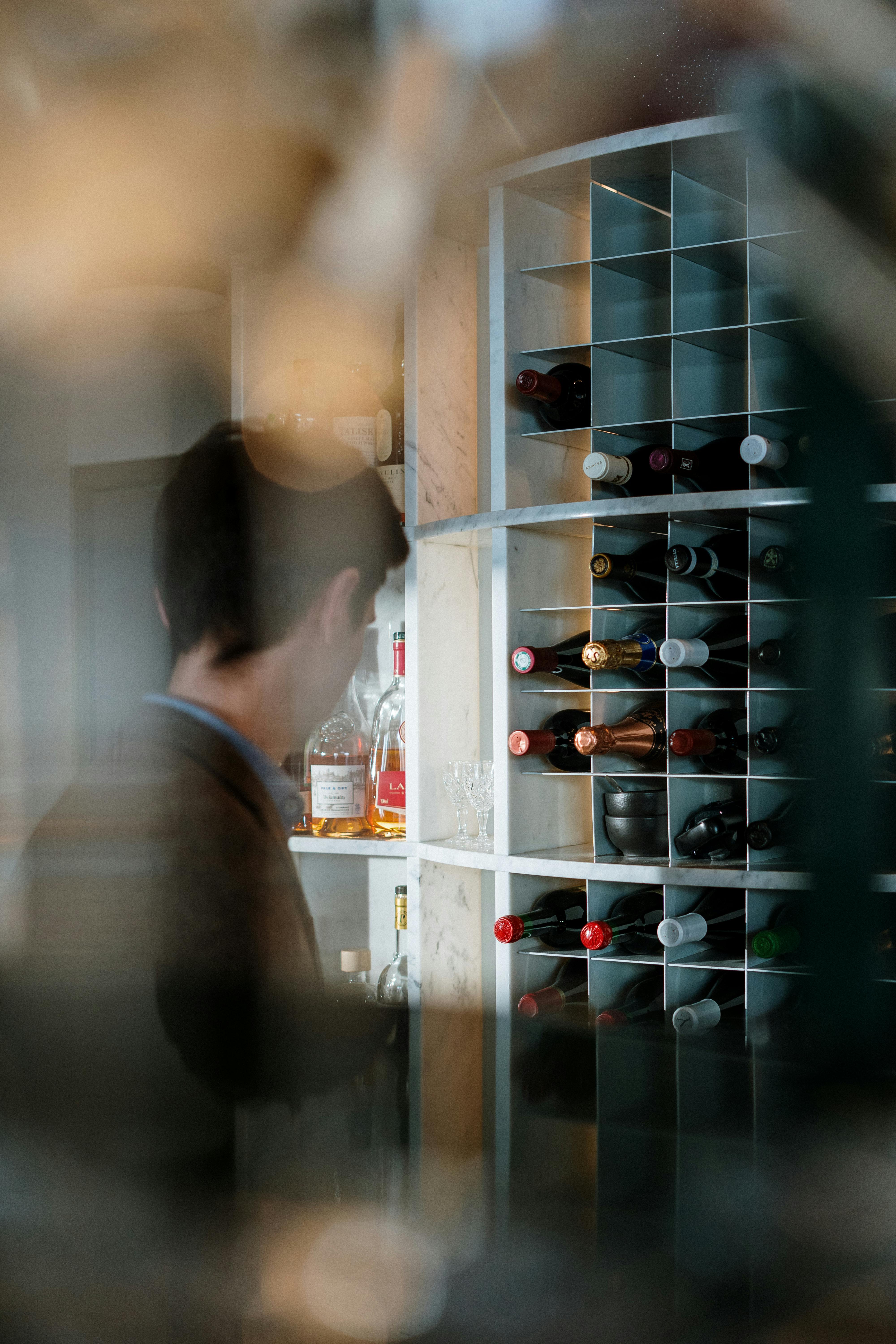 Man in a stylish bar stocks wine bottles in a modern wine rack.