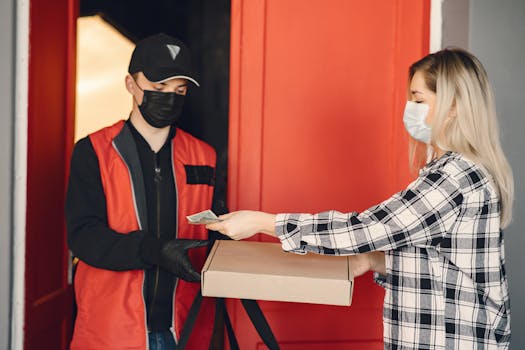 A delivery person in uniform hands over a pizza box to a customer at her door.