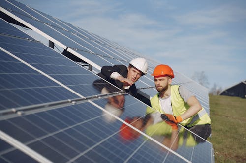 Free Concentrated male coworkers in hardhats working at solar energy station and discussing technical aspects of panels Stock Photo