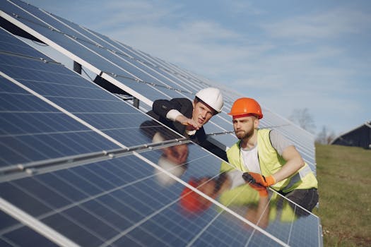 Concentrated male coworkers in hardhats working at solar energy station and discussing technical aspects of panels