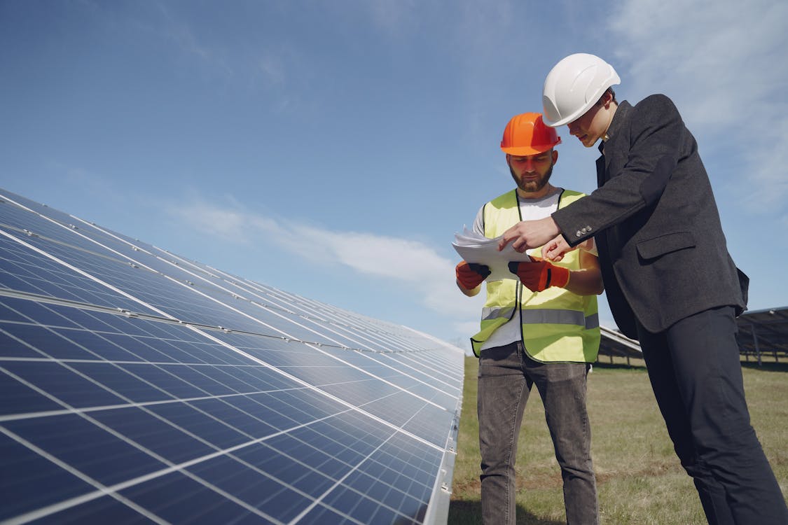 Free Low angle of young inspector and foreman in hardhats checking documentation against modern solar panels in field Stock Photo