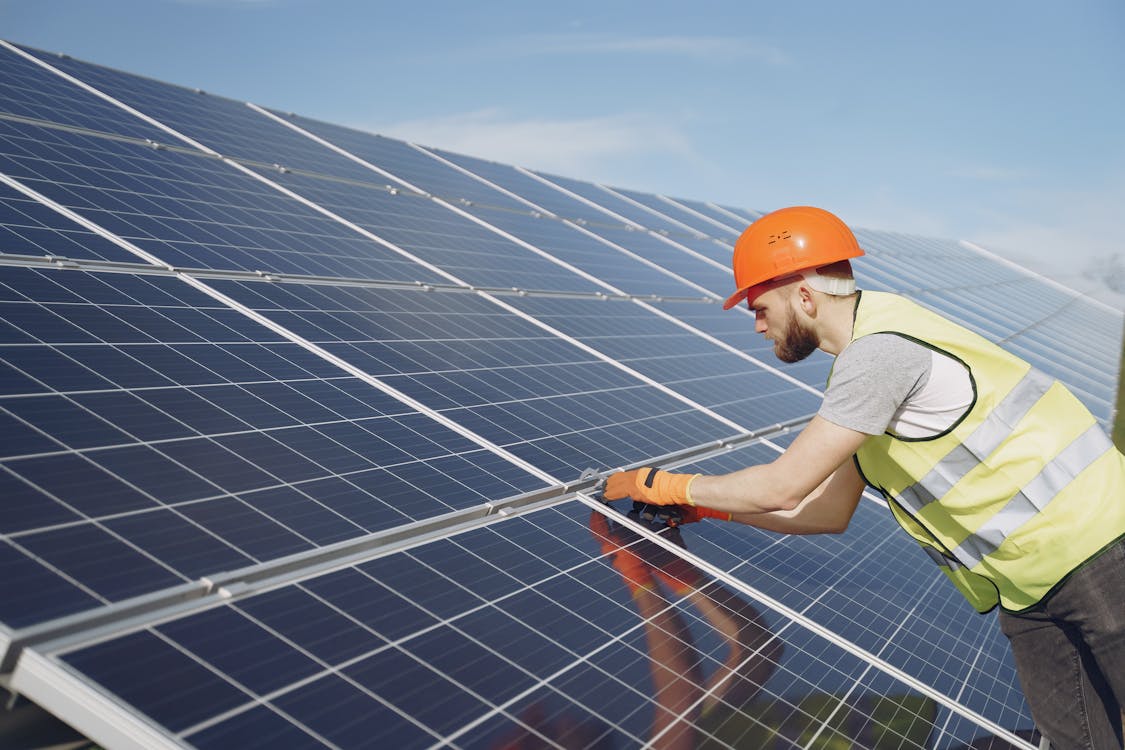 Free Side view of focused young man in uniform and hardhat checking setup of solar panels Stock Photo