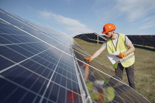 Male supervisor inspecting solar panels on field under blue sky