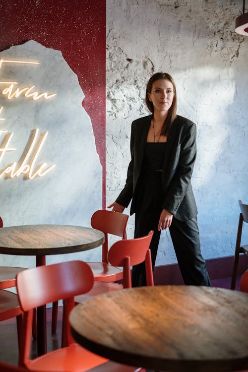 Woman in Black Blazer Standing Beside Brown Wooden Round Table