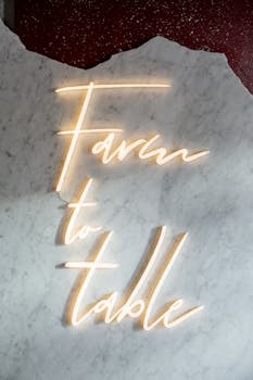 Neon light sign 'Farm to Table' glowing on a marble background, perfect for restaurant theme.