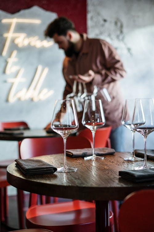 Man in Brown Dress Shirt Sitting Beside Table With Wine Glasses