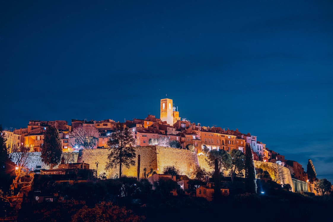 From below of amazing aged Saint Paul de Vence commune with illuminated buildings and ancient bell tower located on hill against evening sky