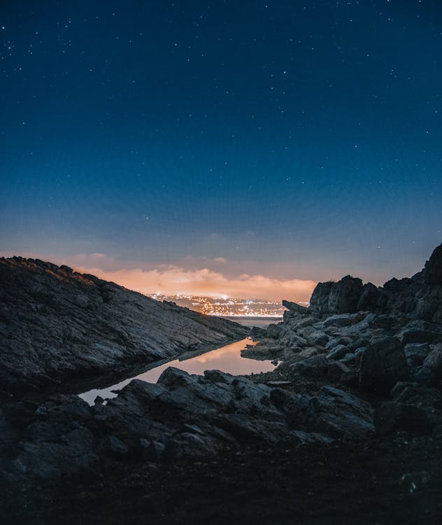Starry sky over rocky cliff and illuminated city