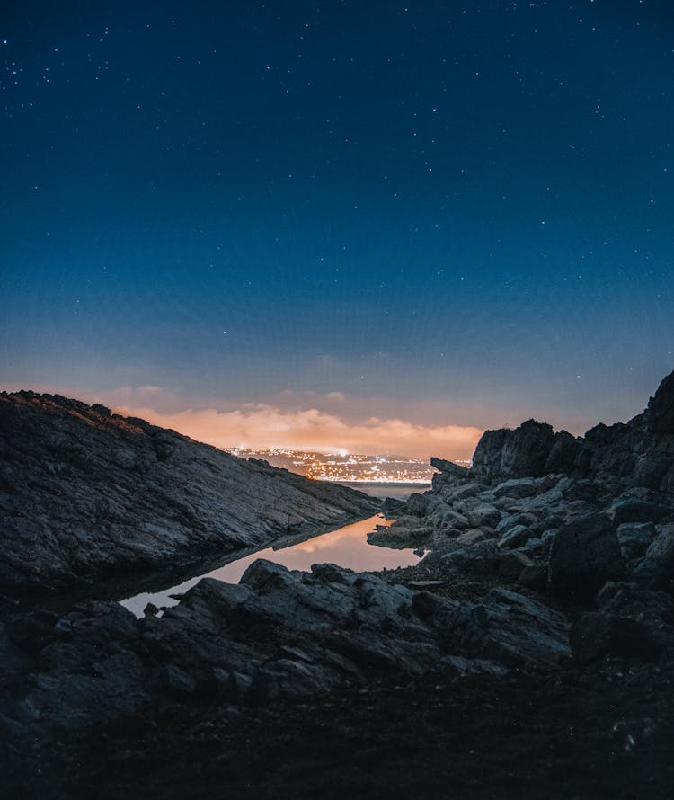 Starry Sky Over Rocky Cliff And Illuminated City