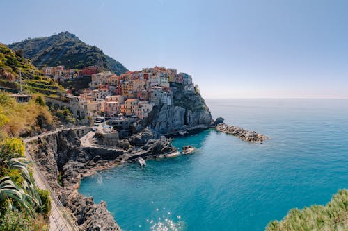 Breathtaking scenery of historic colorful buildings of famous coastal Manarola town located on stony hill in front of turquoise sea on sunny day
