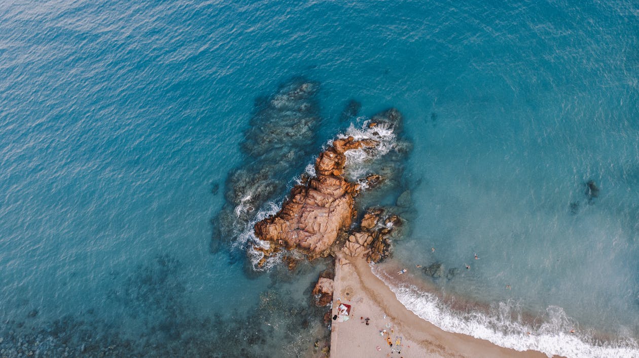 Picturesque drone view of sandy coastline and rock in turquoise sea in daylight