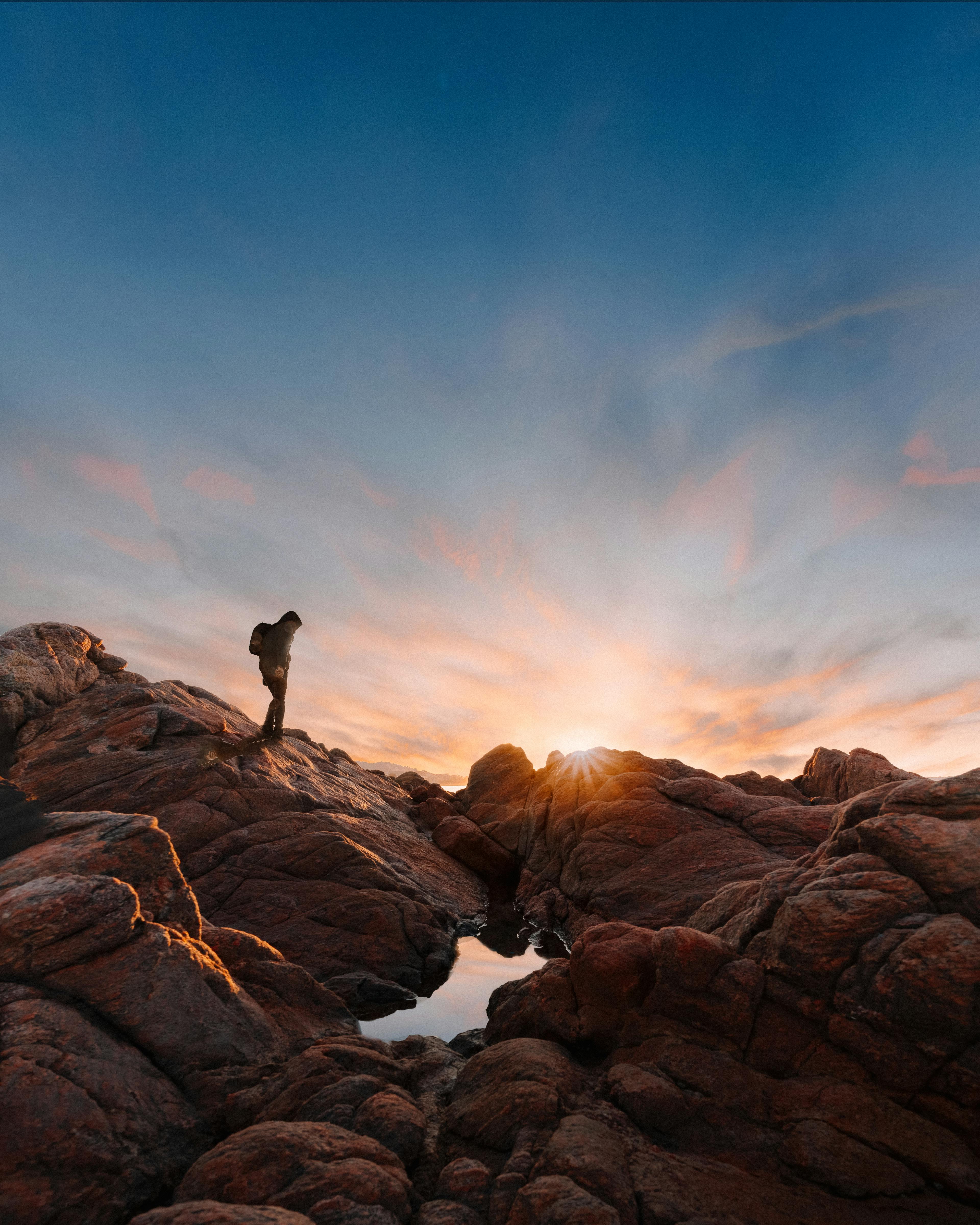 Picturesque view of vibrant sunset above unrecognizable tourist with backpack hiking through rocks