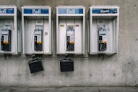 Simple metallic public phones mounted on special box on old grey shabby wall in city in daylight