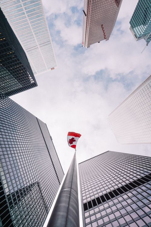Free From below of perspective tunnel between glass skyscrapers and pole with fluttering flag of Canada Stock Photo