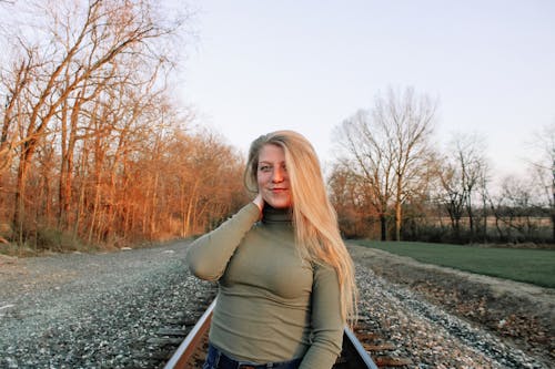 Smiling woman with long hair looking at camera standing on railway in autumnal rural nature